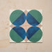 Group image showing four Geometry Ocean 20x20cm geometric patterned tiles arranged to create a circular motif, featuring blue and green semicircles with sand and white corners, photographed against a neutral stone background.