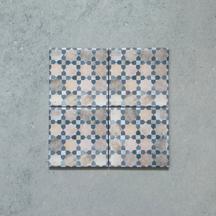 Cuatro azulejos cerámicos de estilo marroquí Bedouin Mequinez Azul 15x15 cm colocados para mostrar el patrón geométrico repetido de estrellas y cruces en tonos azul suave, beige y crema sobre superficie texturizada.