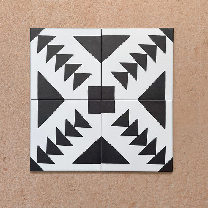 Composición de cuatro azulejos de estilo marroquí Alhambra Alkazar 20x20 cm con motivos triangulares negros sobre fondo blanco definido, formando un impactante patrón geométrico en rombo sobre superficie terracota.
