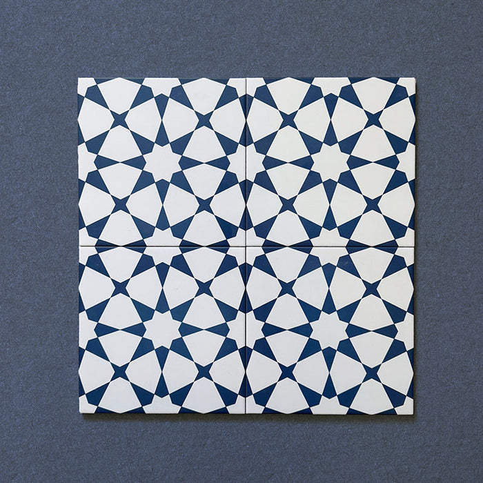 Primer plano de cuatro azulejos cerámicos de estilo marroquí Agraba Azul Marino 20x20 cm colocados juntos, destacando el patrón geométrico de estrellas en azul marino profundo y blanco sobre fondo oscuro texturizado.