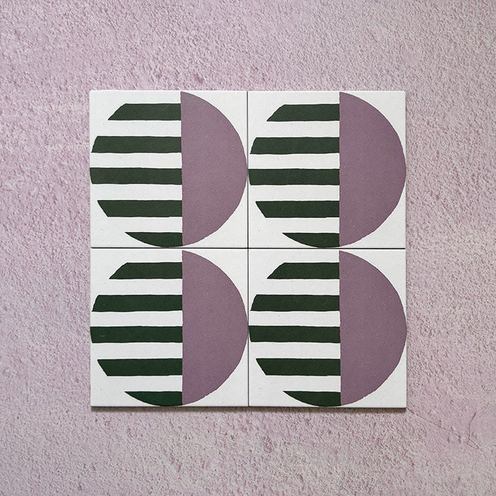 Group image showing four Geometry Seritina 20x20cm patterned tiles arranged to form a circular repeat, featuring green striped semicircles paired with mauve solid semicircles on a cream base, photographed against a textured pink background.