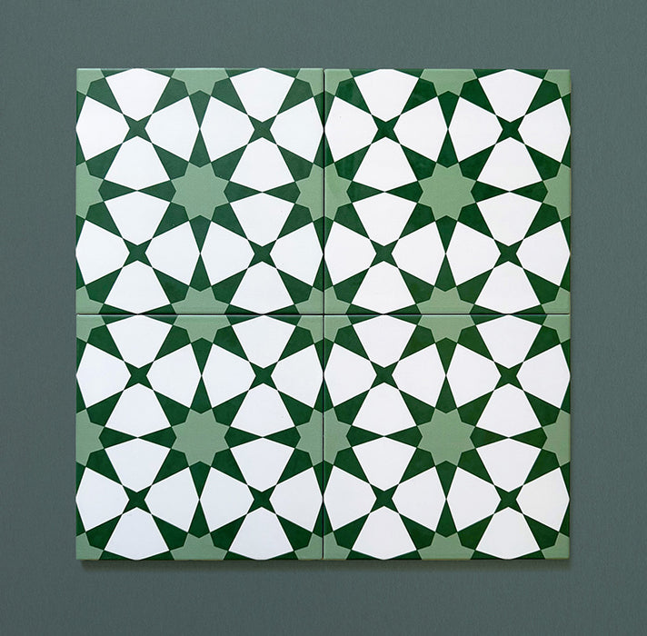 Cuatro azulejos cerámicos de estilo marroquí Agraba Verde 20x20 cm colocados juntos para mostrar la continuidad del patrón geométrico de estrellas en tonos verde intenso y verde suave con detalles blancos sobre fondo verde oscuro.