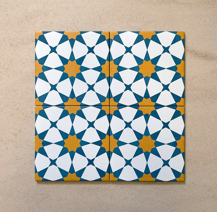 Primer plano de cuatro azulejos cerámicos de estilo marroquí Agraba Sunshine 20x20 cm colocados juntos, destacando un patrón geométrico de estrellas en azul, amarillo mostaza y blanco sobre fondo arena neutro.