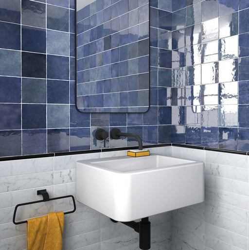 Zona de lavabo en baño con azulejos de pared cerámicos Zellij Azul Cuadrado 13,2 × 13,2 cm de estilo marroquí, mostrando una rica variación en tonos azules con acabado brillante, combinados con lavabo suspendido, grifería negra mate y azulejos inferiores con efecto mármol.