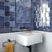 Zona de lavabo en baño con azulejos de pared cerámicos Zellij Azul Cuadrado 13,2 × 13,2 cm de estilo marroquí, mostrando una rica variación en tonos azules con acabado brillante, combinados con lavabo suspendido, grifería negra mate y azulejos inferiores con efecto mármol.