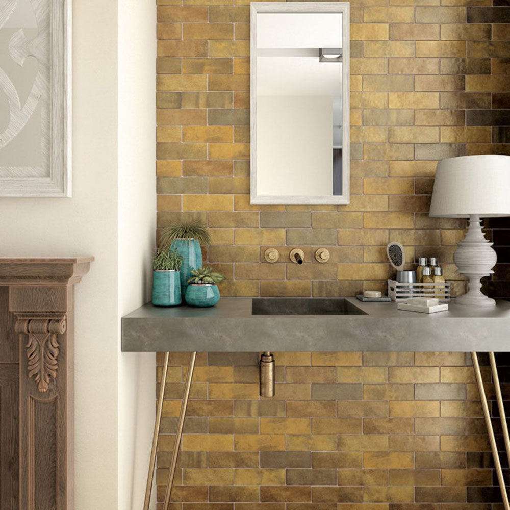 Interior de baño con azulejos de pared cerámicos Zellij Dorado Ladrillo 6,5 × 20 cm de estilo marroquí, colocados en un diseño tipo ladrillo clásico con tonos dorados cálidos, variación natural y un acabado brillante de aspecto artesanal, combinados con grifería de latón y un mueble de lavabo de hormigón para un resultado rico en textura.