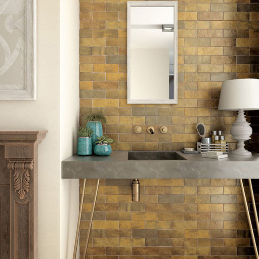 Interior de baño con azulejos de pared cerámicos Zellij Dorado Ladrillo 6,5 × 20 cm de estilo marroquí, colocados en un diseño tipo ladrillo clásico con tonos dorados cálidos, variación natural y un acabado brillante de aspecto artesanal, combinados con grifería de latón y un mueble de lavabo de hormigón para un resultado rico en textura.