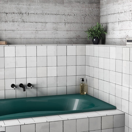 Interior de baño con azulejos de pared cerámicos Zellij Blanco Cuadrado 13,2 × 13,2 cm de estilo marroquí, colocados en un diseño en cuadrícula, con sutil variación tonal y efecto artesanal, combinado con bañera verde, grifería negra y paredes de hormigón.