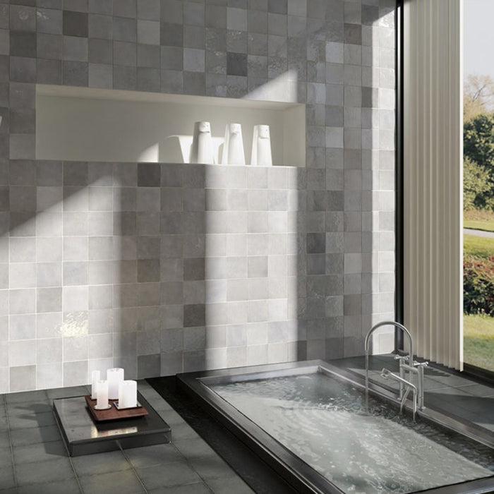 Interior de baño con azulejos de pared cerámicos Zellij Blanco Cuadrado 13,2 × 13,2 cm de estilo marroquí, colocados en un diseño en cuadrícula, con sutil variación tonal y efecto artesanal, combinado con bañera integrada, estante empotrado y luz natural.