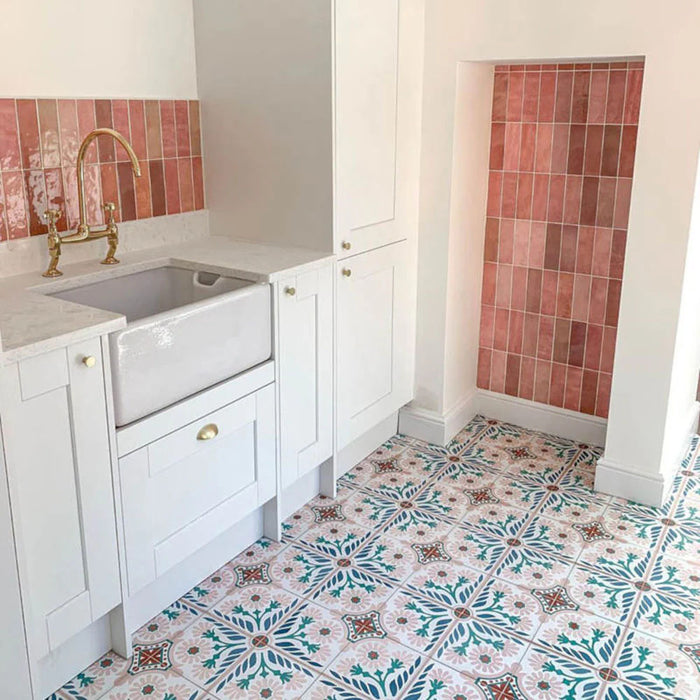 Cocina con azulejos porcelánicos Sakura Rose 20 × 20 cm de estilo marroquí para suelo, mostrando un patrón floral decorativo en tonos rosa suave, verde azulado y terracota, combinados con azulejos tipo ladrillo en rosa empolvado y mobiliario blanco estilo shaker.