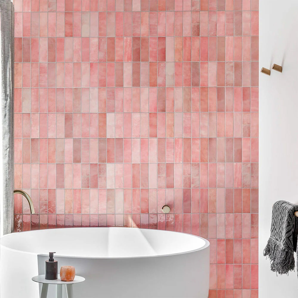 Interior de baño con azulejos de pared cerámicos Zellij Pink Brick 6,5 × 20 cm de estilo marroquí, mostrando una suave variación tonal en rosa y una textura brillante de aspecto artesanal, combinados con bañera exenta blanca, grifería de latón cepillado y una decoración neutra y suave.