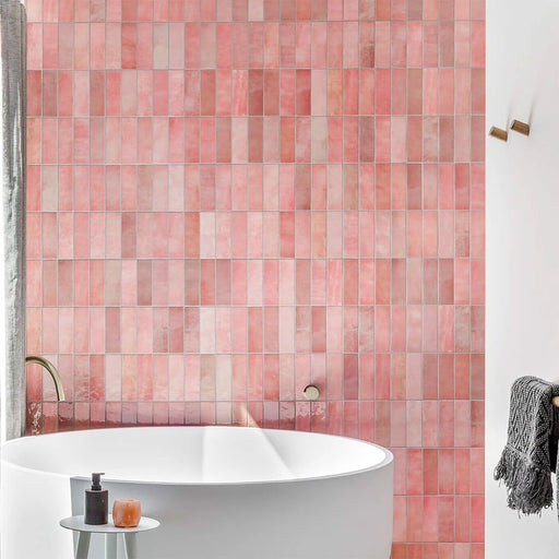 Interior de baño con azulejos de pared cerámicos Zellij Pink Brick 6,5 × 20 cm de estilo marroquí, mostrando una suave variación tonal en rosa y una textura brillante de aspecto artesanal, combinados con bañera exenta blanca, grifería de latón cepillado y una decoración neutra y suave.
