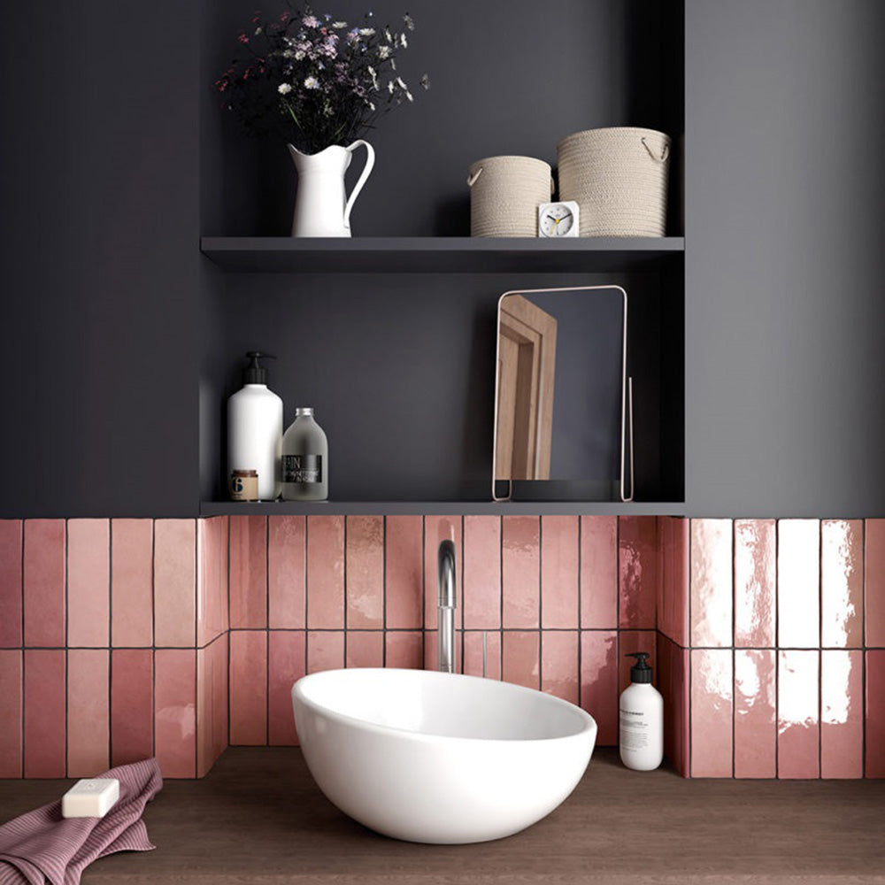 Interior de baño con azulejos de pared cerámicos Zellij Rosa Ladrillo 6,5 × 20 cm de estilo marroquí en tonos rosa suaves, colocados en un diseño tipo ladrillo con acabado brillante, combinados con lavabo blanco, estanterías oscuras y accesorios modernos para un acabado cálido y contemporáneo.