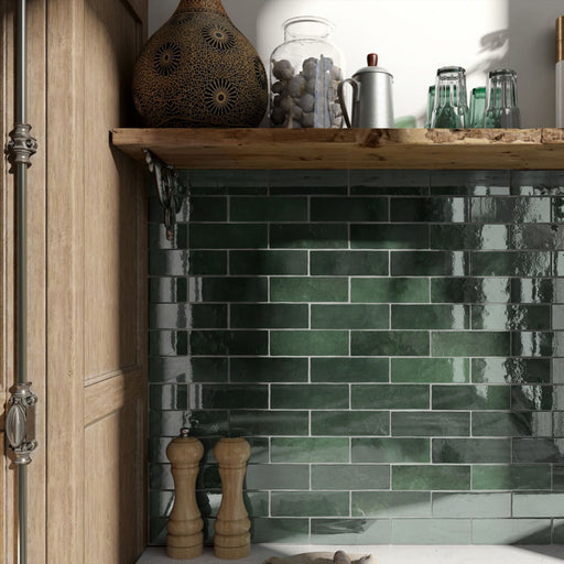 Salpicadero de cocina con azulejos de pared cerámicos Zellij Verde Musgo Ladrillo 6,5 × 20 cm de estilo marroquí, colocados en un diseño tipo ladrillo clásico con rica variación en tonos verdes, acabado brillante de aspecto artesanal y bordes suavemente irregulares, combinados con estanterías de madera cálida y materiales naturales para aportar profundidad y contraste.
