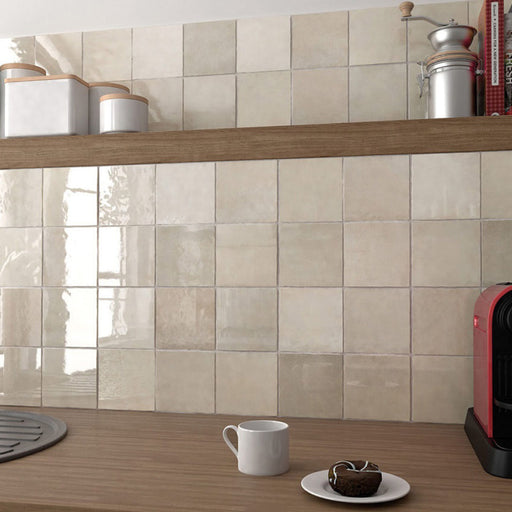 Interior de cocina con azulejos de pared cerámicos Zellij Ocre Cuadrado 13,2 × 13,2 cm de estilo marroquí en tonos neutros cálidos, colocados como salpicadero en formato cuadrado con acabado brillante, combinados con estanterías de madera, accesorios de encimera y luz natural suave.