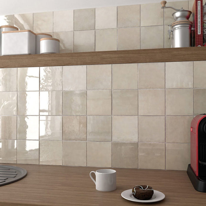 Interior de cocina con azulejos de pared cerámicos Zellij Ocre Cuadrado 13,2 × 13,2 cm de estilo marroquí en tonos neutros cálidos, colocados como salpicadero en formato cuadrado con acabado brillante, combinados con estanterías de madera, accesorios de encimera y luz natural suave.