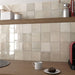 Interior de cocina con azulejos de pared cerámicos Zellij Ocre Cuadrado 13,2 × 13,2 cm de estilo marroquí en tonos neutros cálidos, colocados como salpicadero en formato cuadrado con acabado brillante, combinados con estanterías de madera, accesorios de encimera y luz natural suave.