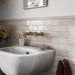 Interior de baño con azulejos de pared cerámicos Zellij Ocre Ladrillo 6,5 × 20 cm de estilo marroquí en tonos neutros cálidos, colocados en un diseño tipo ladrillo con acabado brillante, combinados con grifería de latón empotrada en pared, lavabo blanco y luz natural suave.