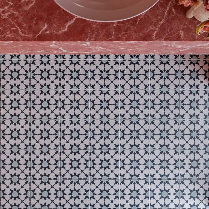 Azulejos de suelo Agraba Azul Blue de 20 × 20 cm de estilo marroquí, con un patrón geométrico de estrellas en azul y blanco que se repite por toda la superficie, combinados con un llamativo lavabo de mármol rosa.