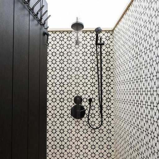 Interior de ducha con azulejos cerámicos de estilo marroquí Agraba Blanco y Negro 20x20 cm para pared, mostrando un clásico patrón geométrico en blanco y negro, combinados con grifería negra mate en un baño contemporáneo.