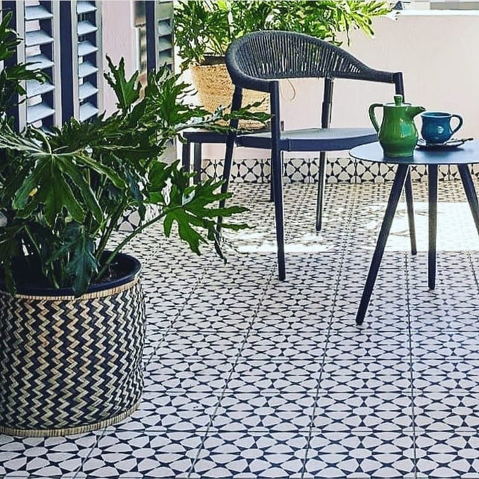 Terraza exterior con azulejos cerámicos de estilo marroquí Agraba Blanco y Negro 20x20 cm para suelo, combinados con mobiliario azul marino y grandes macetas con plantas verdes.