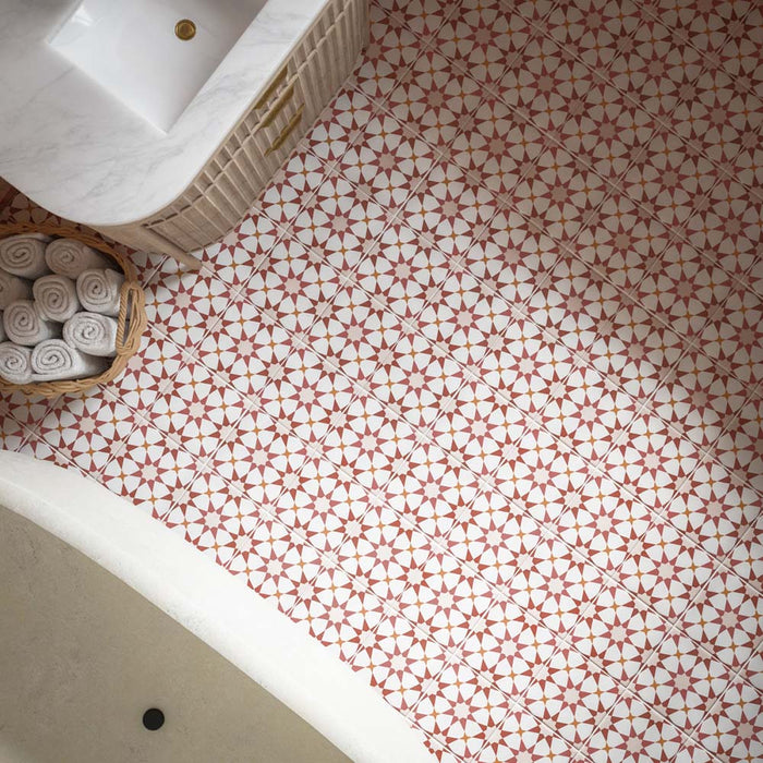Baño con azulejos de suelo Agraba Cotto de 20 × 20 cm de estilo marroquí, combinados con azulejos de pared a rayas en tonos terracota, una bañera exenta, paredes en tonos neutros y cálidos detalles en latón.