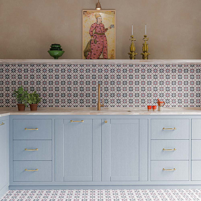 Azulejos Agraba Mini Atlas de 15 × 15 cm de estilo marroquí, con un patrón geométrico repetitivo en suaves tonos azul, burdeos y blanco, instalados tanto en el salpicadero como en el suelo de la cocina y combinados con muebles en azul claro y detalles en latón.