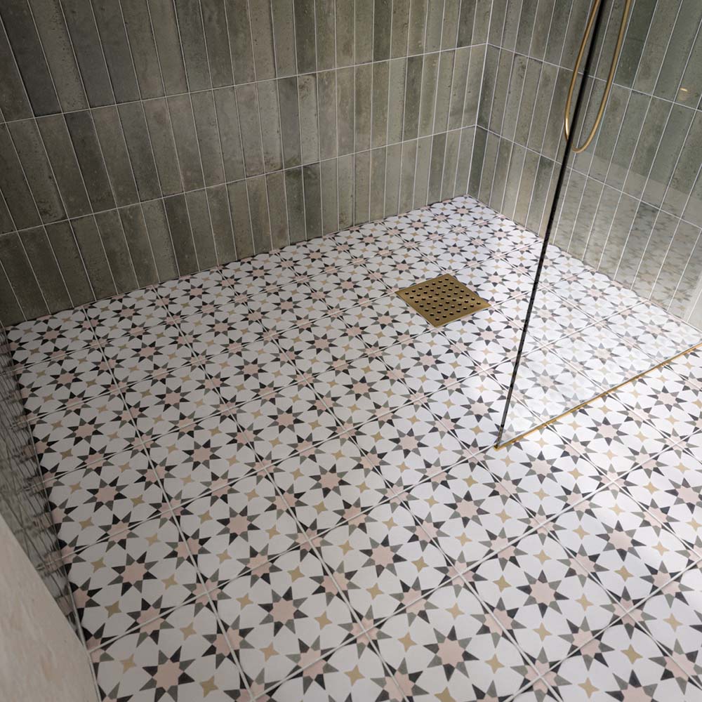 Ducha a ras de suelo con azulejos Agraba Natural de estilo marroquí en el suelo, combinados con azulejos de pared en tono verde salvia colocados en vertical, una mampara de cristal sin marco y grifería de ducha en acabado latón cepillado para crear un baño contemporáneo de inspiración mediterránea.