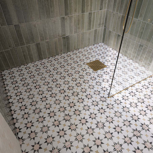 Ducha a ras de suelo con azulejos Agraba Natural de estilo marroquí en el suelo, combinados con azulejos de pared en tono verde salvia colocados en vertical, una mampara de cristal sin marco y grifería de ducha en acabado latón cepillado para crear un baño contemporáneo de inspiración mediterránea.