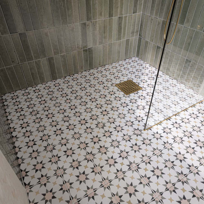 Ducha a ras de suelo con azulejos Agraba Natural de estilo marroquí en el suelo, combinados con azulejos de pared en tono verde salvia colocados en vertical, una mampara de cristal sin marco y grifería de ducha en acabado latón cepillado para crear un baño contemporáneo de inspiración mediterránea.