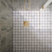 Ducha a ras de suelo con azulejos Agraba Natural de estilo marroquí en el suelo, combinados con azulejos de pared en tono verde salvia colocados en vertical, una mampara de cristal sin marco y grifería de ducha en acabado latón cepillado para crear un baño contemporáneo de inspiración mediterránea.