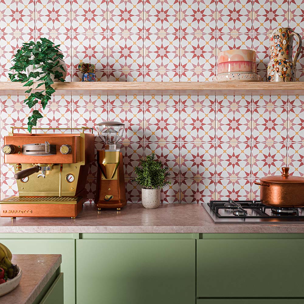 Cocina llena de color con azulejos decorados Agraba Springs de 20 × 20 cm de estilo marroquí en el salpicadero, con motivos geométricos de estrellas en tonos rosa, terracota y crema, combinados con muebles en verde salvia, utensilios de cocina de cobre y estanterías de madera.