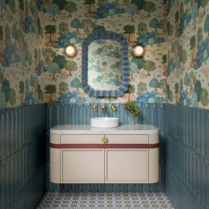 Azulejos Agraba Sunshine de 20 × 20 cm de estilo marroquí, con un elaborado patrón geométrico en azul, blanco y cálidos tonos ocre en el suelo del baño, combinados con azulejos de pared azules con relieve y papel pintado de motivos botánicos.