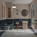 Baño lleno de color con azulejos de suelo Agraba Blue and Yellow de 20 × 20 cm de estilo marroquí, con motivos geométricos de estrellas en tonos azul, naranja y crema, combinados con azulejos de pared brillantes en azul intenso, un lavabo acanalado en color crema y grifería en acabado latón.