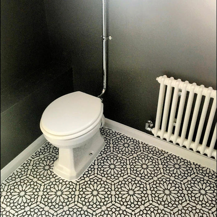 Baño con azulejos cerámicos de estilo marroquí Alhambra Hexagon 18,7x21,6 cm para suelo en blanco y negro, creando una marcada declaración geométrica, combinados con paredes gris oscuro, inodoro blanco y radiador clásico para contraste.