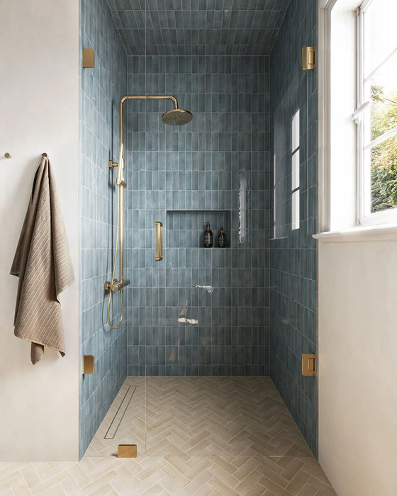Baño con azulejos de pared Atlas Blue Mini Brick 5x15 cm en acabado brillo, instalados en disposición vertical en las paredes de la ducha y en nichos integrados, mostrando tonos azules intensos con una sutil variación tonal, combinados con grifería en latón y un suelo en espiga en tonos claros para un acabado refinado.