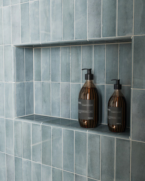 Baño con azulejos de pared Atlas Blue Mini Brick 5x15 cm en acabado brillo, instalados en disposición vertical en las paredes de la ducha y en nichos integrados, mostrando tonos azules intensos con una sutil variación tonal, combinados con grifería en latón y un suelo en espiga en tonos claros para un acabado refinado.
