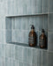 Baño con azulejos de pared Atlas Blue Mini Brick 5x15 cm en acabado brillo, instalados en disposición vertical en las paredes de la ducha y en nichos integrados, mostrando tonos azules intensos con una sutil variación tonal, combinados con grifería en latón y un suelo en espiga en tonos claros para un acabado refinado.