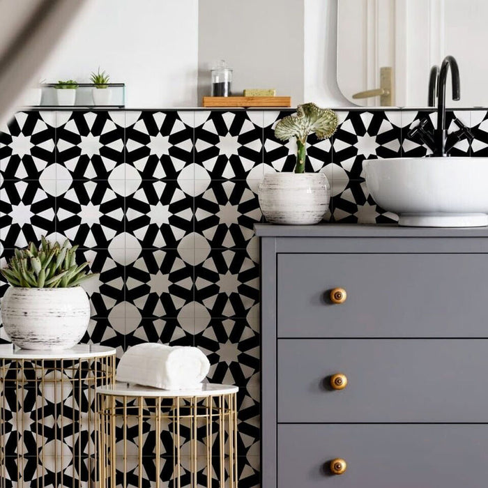 Interior de baño con azulejos cerámicos de estilo marroquí Alhambra Mini Jemia 15x15 cm para pared, mostrando un audaz patrón geométrico en blanco y negro colocado detrás de un mueble gris con detalles en latón y grifería negra mate.