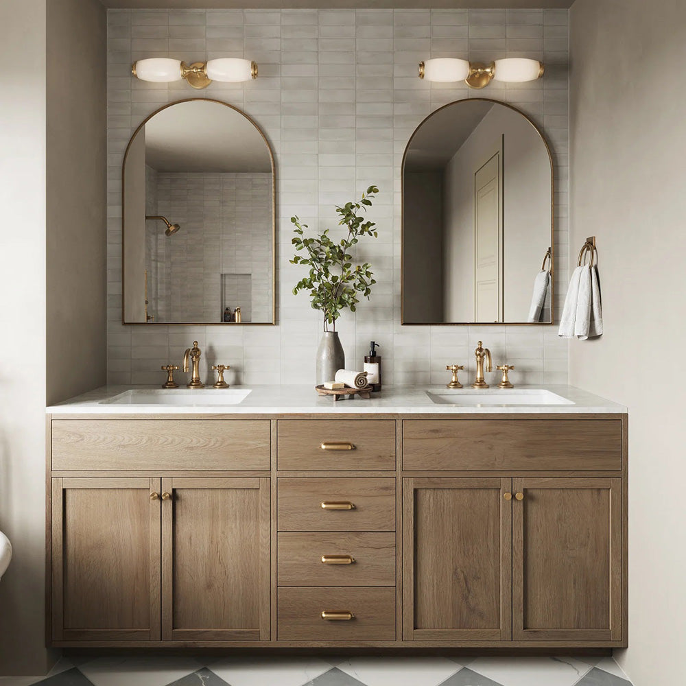 Baño con azulejos de pared Atlas White Mini Brick 5x15 cm en acabado mate, colocados en disposición horizontal tipo ladrillo para crear un fondo suave y texturizado. La sutil variación tonal y el acabado mate refinado aportan una sensación tranquila y discreta, combinados con mobiliario de madera cálida, grifería en latón y espejos arqueados para un estilo contemporáneo equilibrado.