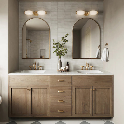 Baño con azulejos de pared Atlas White Mini Brick 5x15 cm en acabado mate, colocados en disposición horizontal tipo ladrillo para crear un fondo suave y texturizado. La sutil variación tonal y el acabado mate refinado aportan una sensación tranquila y discreta, combinados con mobiliario de madera cálida, grifería en latón y espejos arqueados para un estilo contemporáneo equilibrado.