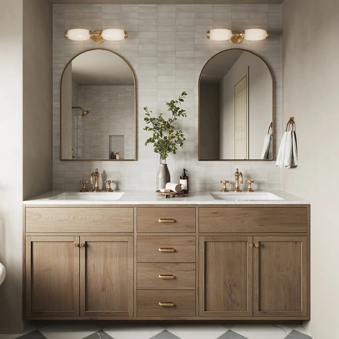 Baño con azulejos de pared Atlas White Mini Brick 5x15 cm en acabado mate, colocados en disposición horizontal tipo ladrillo para crear un fondo suave y texturizado. La sutil variación tonal y el acabado mate refinado aportan una sensación tranquila y discreta, combinados con mobiliario de madera cálida, grifería en latón y espejos arqueados para un estilo contemporáneo equilibrado.