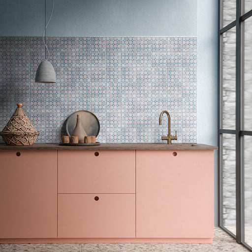 Cocina con azulejos de pared decorados Bedouin Mequinez Blue de 15 × 15 cm, de estilo marroquí y con un delicado diseño geométrico azul, combinados con muebles en un suave tono rosa, cálidos detalles en madera y grifería en acabado latón.