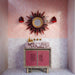 Baño con azulejos Bedouin Mequinez Rose de estilo marroquí para paredes y suelo, combinados con azulejos Atlas Pink Mini Brick Gloss colocados en patrón de espiga. Decorado con un lavabo efecto mármol en tonos rosa, grifería en acabado latón, un espejo decorativo tipo sol y cálidos tonos rosados que crean un espacio atrevido y lleno de personalidad.