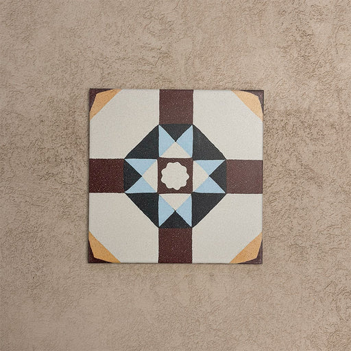Baldosa Europa Berlin 20×20 cm de estilo Victoriano Marroquí mostrada individualmente sobre un fondo beige texturizado, con patrón geométrico en forma de estrella en tonos burdeos, azul, mostaza y crema en una imagen de producto en primer plano.