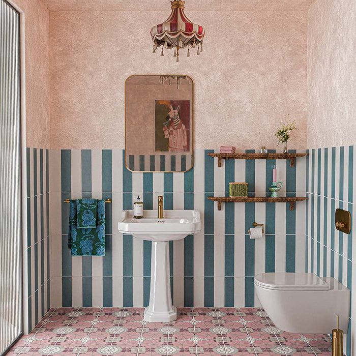Baño con azulejos de suelo Nantes Rose Pink de 20 × 20 cm, con un diseño decorativo de estilo marroquí, combinados con azulejos de pared a rayas en verde azulado y blanco, paredes rosas con textura, un lavabo con pedestal y detalles en latón.