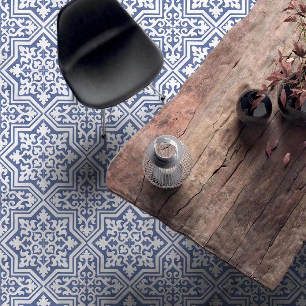 Interior de comedor con baldosas de suelo Europa Trondheim Blue 20 × 20 cm de estilo Victoriano Marroquí en tonos azul y blanco, combinadas con una mesa rústica de madera, una silla negra y accesorios decorativos en un entorno interior contemporáneo.