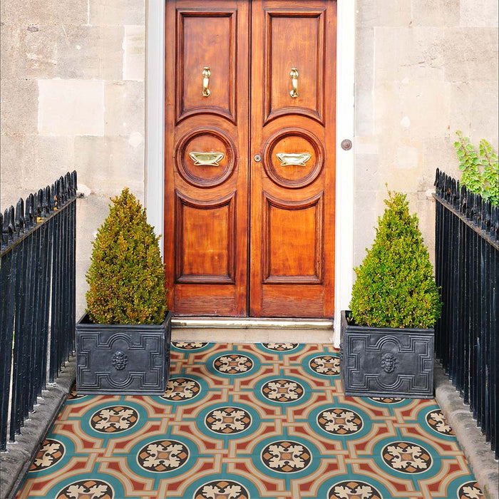 Entrada con baldosas de suelo Europa Helsinki 20 × 20 cm de estilo Victoriano Marroquí en tonos verde azulado, terracota y crema, instaladas en un porche decorativo con puertas de madera, paredes de piedra y plantas en maceta.