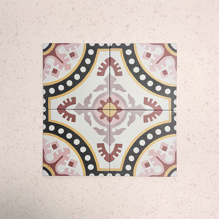 Cuatro baldosas Europa Dortmund 20 × 20 cm de estilo Victoriano Marroquí colocadas juntas para mostrar el patrón decorativo repetitivo en tonos rojo, crema, negro y mostaza, sobre un fondo rosa empolvado texturizado.