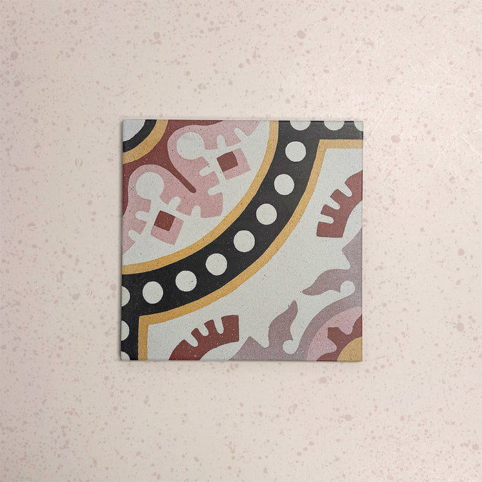 Baldosa Europa Dortmund 20 × 20 cm de estilo Victoriano Marroquí mostrada individualmente sobre un fondo rosa empolvado texturizado, con un patrón decorativo geométrico y floral en esquina en tonos rojo, crema, negro y mostaza en una imagen de producto en primer plano.
